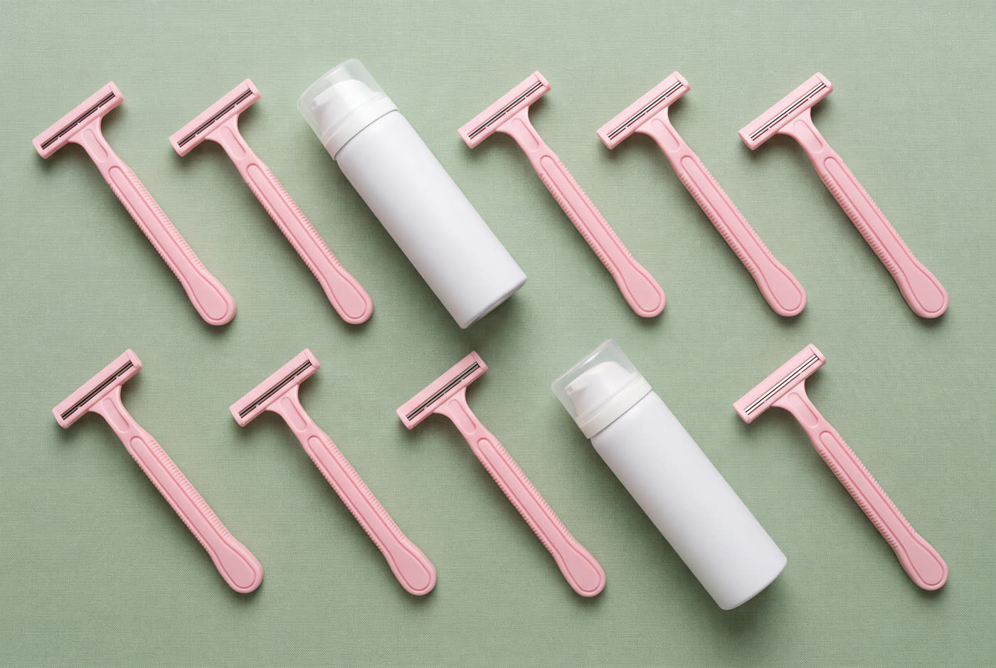 Pink disposable razors and shaving cream cans tiled on a sage green background