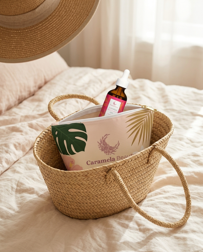 Caramela tropical pouch with the oil bottle peeking out, packed in a straw tote on a bed